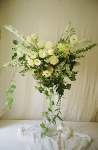 an arrangement of white flowers and greenery on a table