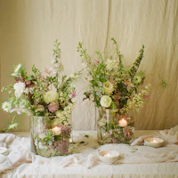 two glass vases filled with flowers and candles